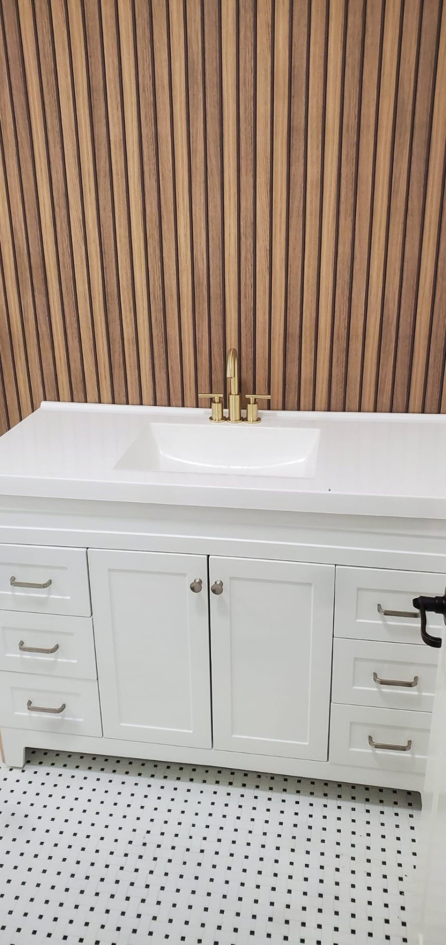 Finished white vanity with cultured-marble top, brass faucet and slat accent wall